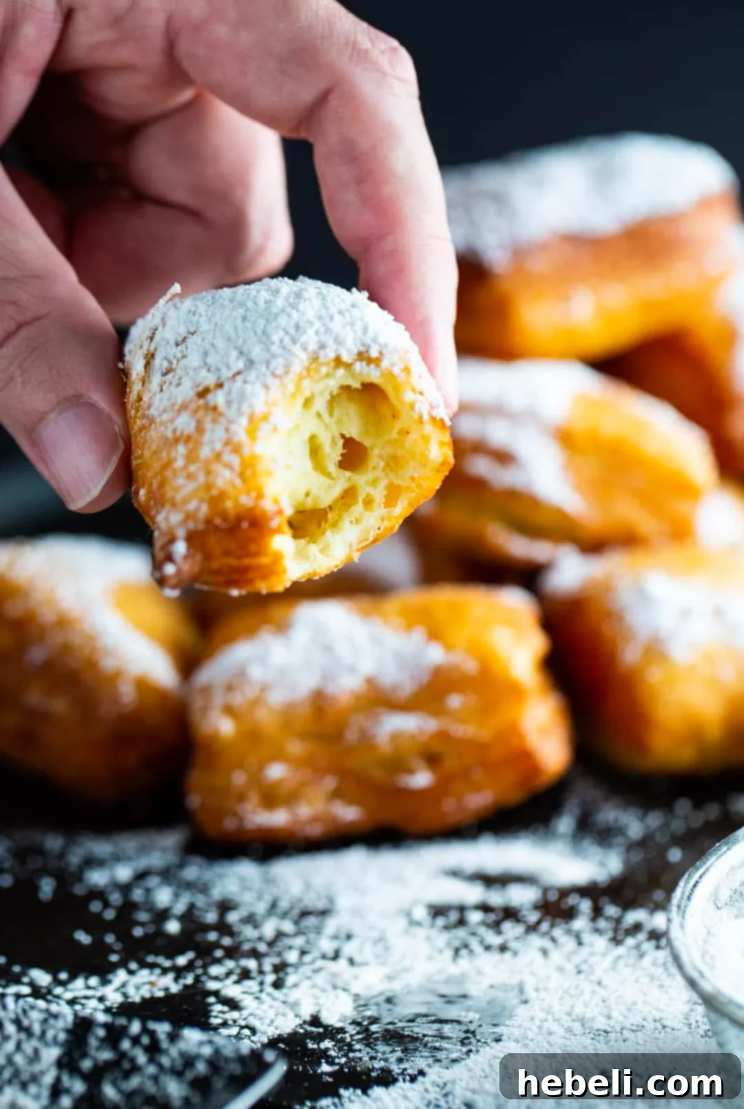 Pillowy Homemade Beignets 6 A hand holding a half-eaten homemade beignet, showing its fluffy interior.