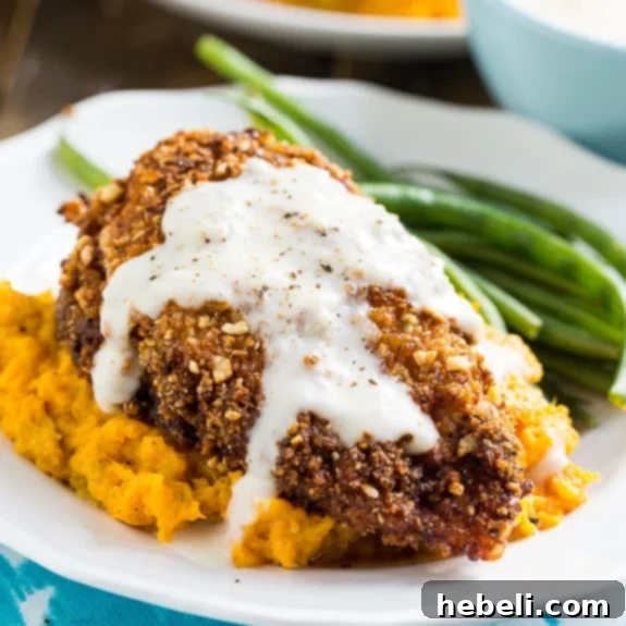 Nutty Fried Chicken with Smashed Sweet Potatoes and Milk Gravy - Golden-brown chicken breast on a bed of vibrant sweet potatoes.