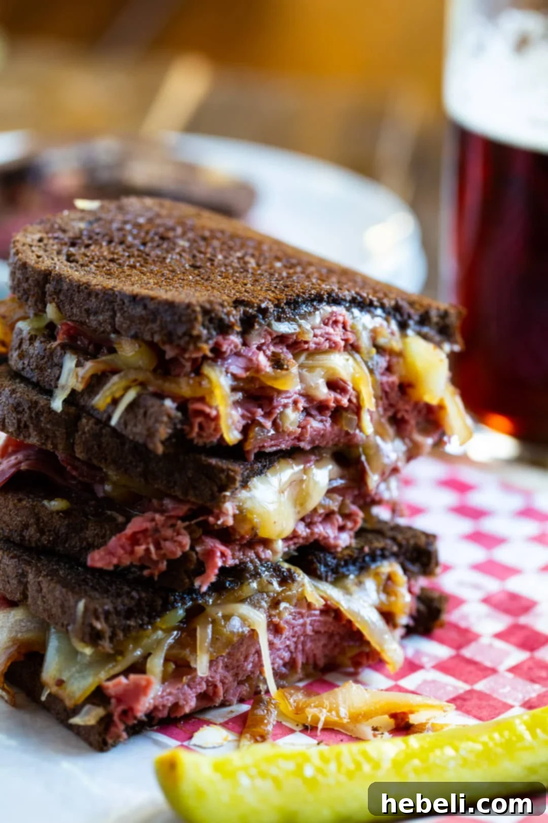 The Sizzling Corned Beef Melt 3 A half of a Grilled Cheese sandwich stacked on another half, accompanied by a pickle spear.