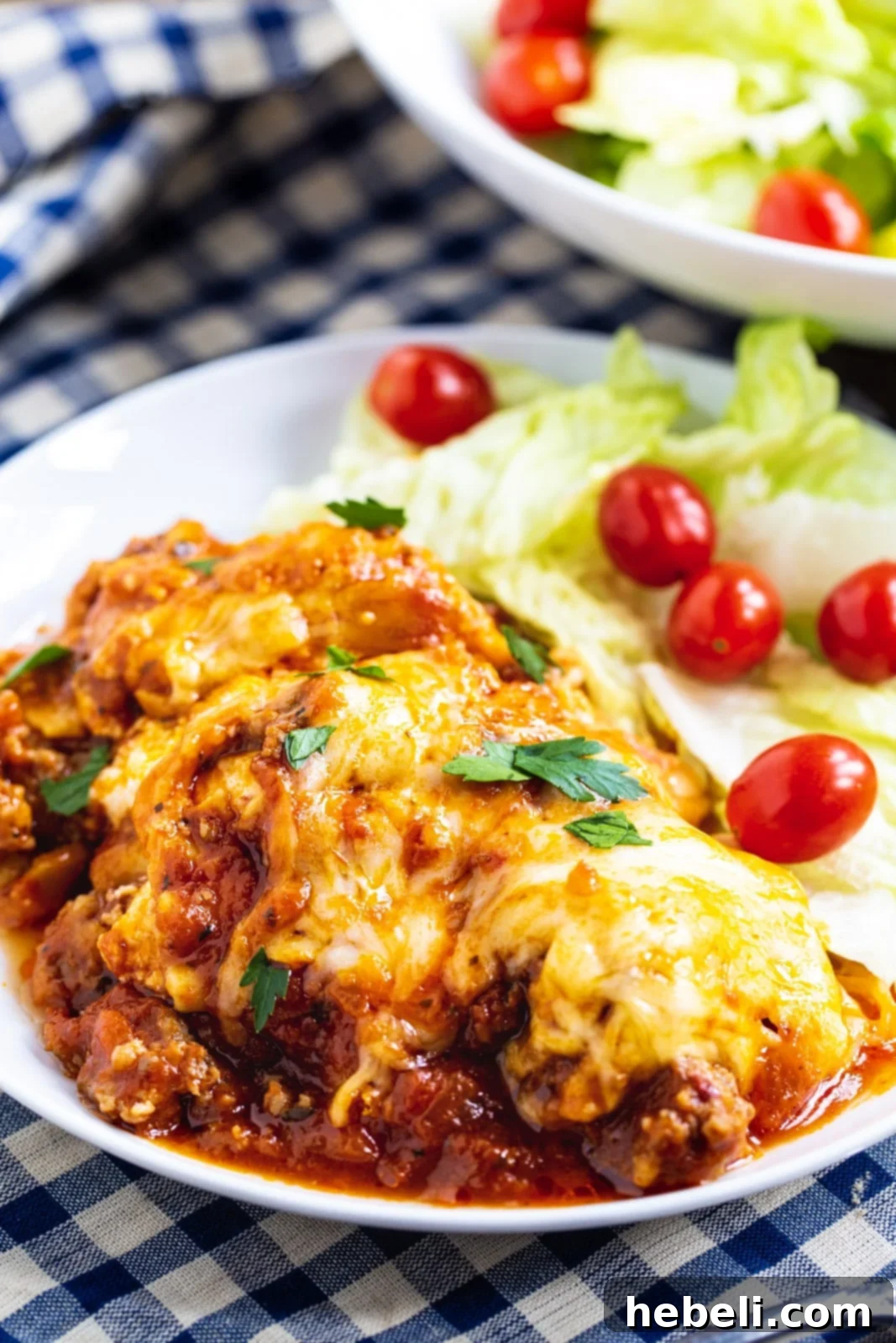A generous serving of slow cooker lasagna on a white plate, accompanied by a fresh green salad.