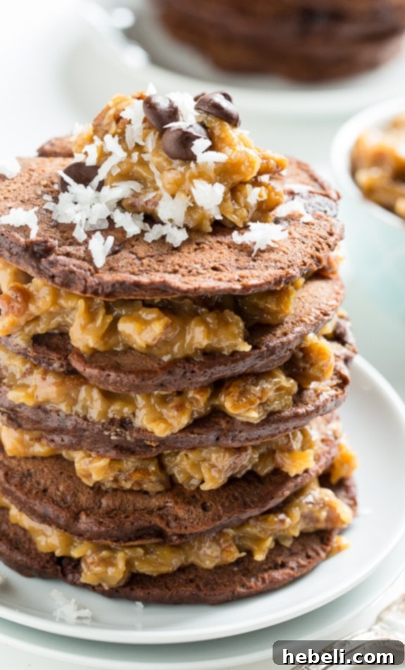 Decadent German Chocolate Pancakes 3 Close-up of fluffy chocolate pancakes layered with thick, golden-brown coconut pecan syrup, showing off the textures of coconut and chopped pecans.