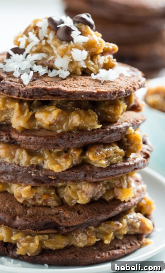 Decadent German Chocolate Pancakes 6 Artfully arranged German Chocolate Pancakes on a white plate, ready to be served, with a spoon of the decadent coconut pecan syrup on the side.
