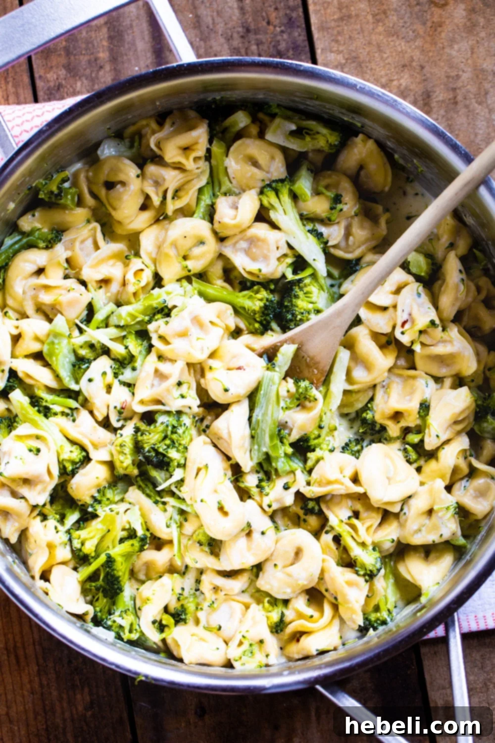 Close-up of cooked tortellini and vibrant green broccoli florets simmering in a creamy sauce in a large pot.