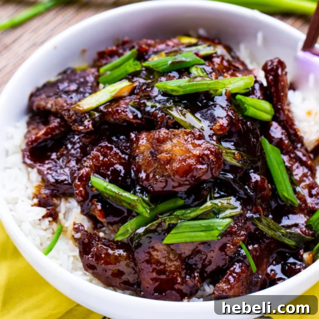 Mongolian Beef served over white rice in a ceramic bowl, garnished with green onions.