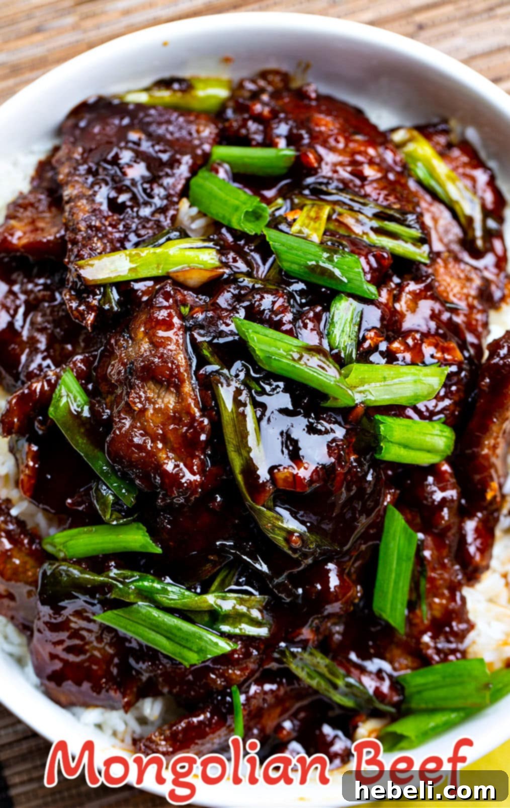 A bowl of Mongolian Beef with white rice, garnished with fresh green onions, ready to eat.