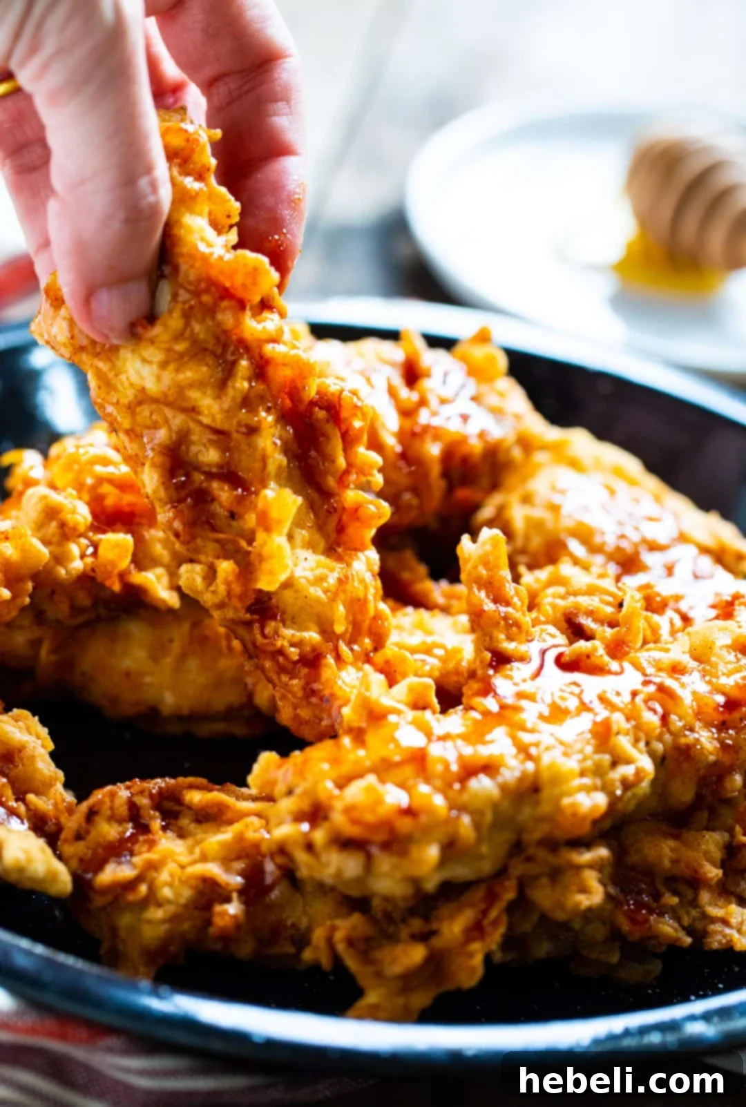 A hand reaching for a Honey Chipotle Chicken Crisper from a serving bowl.