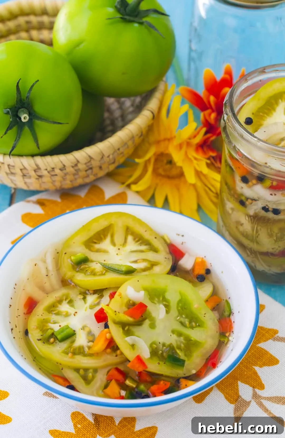 Pickled Green Tomatoes in a bowl with whole green tomatoes in background.
