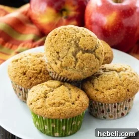 Muffins on a white plate with apples in background.